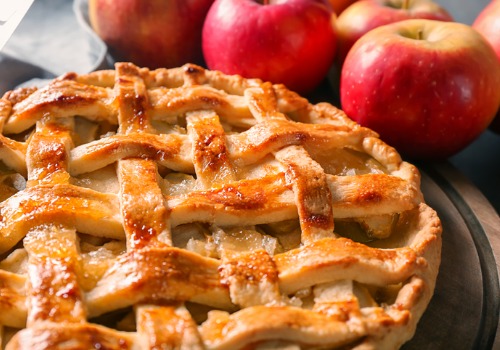 freshly baked apple pie on a table next to red apples