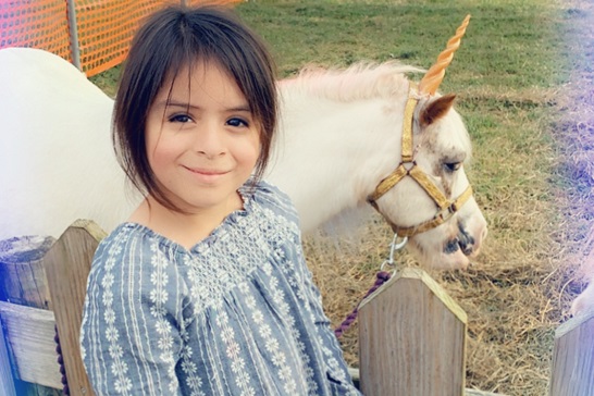 A young girls smiles with a unicorn behind her at Tanners Orchard, which offers numerous events such as a Sunflower Festival for Aurora IL residents