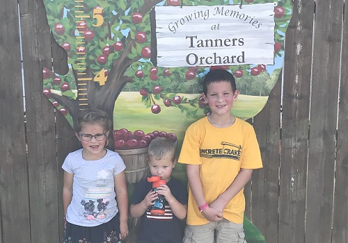 Children stand in front of a sign for Tanners Orchard, an Event Venue by Dunlap IL
