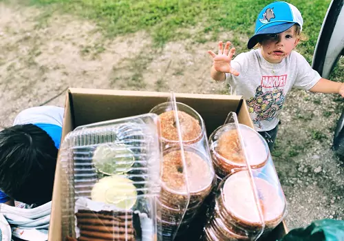 A child waves at his parent, who is holding a box of apple cider donuts at Tanners Orchard, which offers Kids Activities for Champaign IL residents